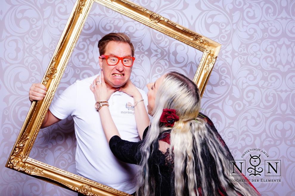 Hochzeitsgäste albern mit goldenem Bilderrahmen an der Fotobox herum