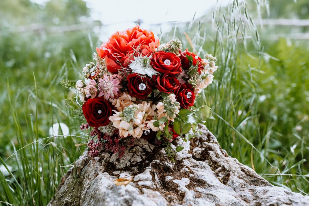 Roter Brautstrauß mit Rosen auf einem Stein im hohen Gras